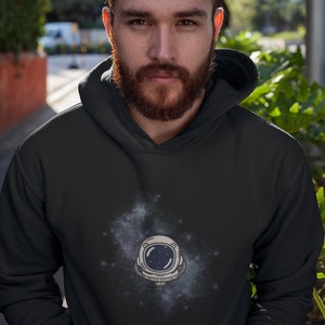 May include: A black hooded sweatshirt with a white astronaut helmet graphic in a galaxy design.