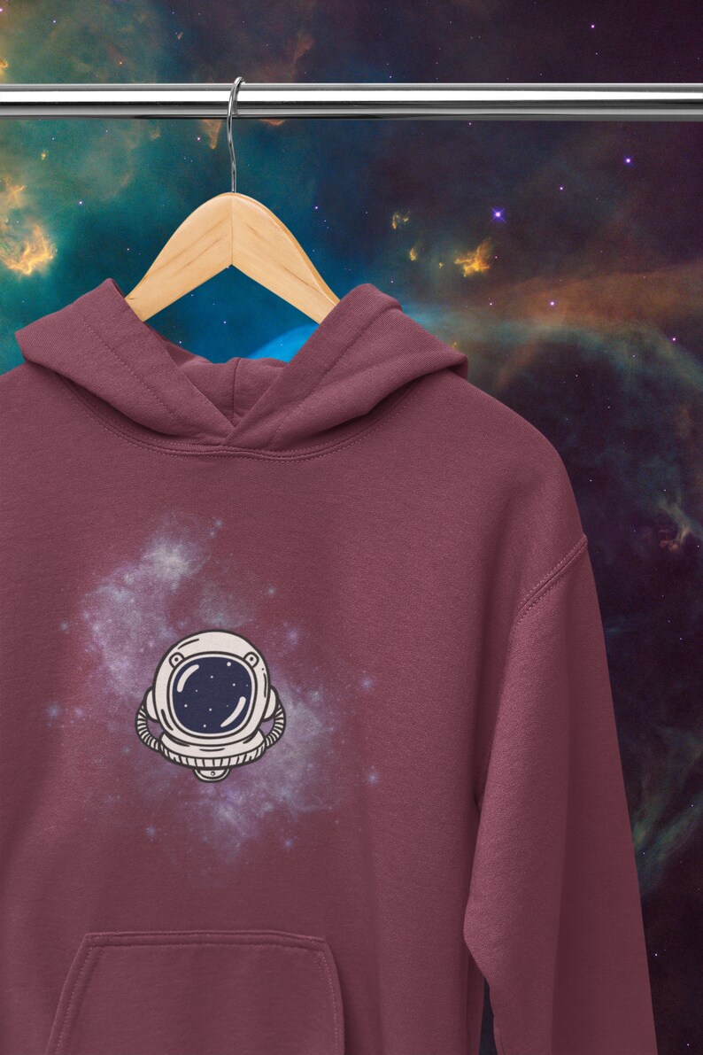 May include: A maroon hoodie with a white astronaut helmet graphic on the front. The graphic is surrounded by a white galaxy design.