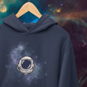 May include: A navy blue hoodie with a white astronaut helmet graphic against a galaxy background.