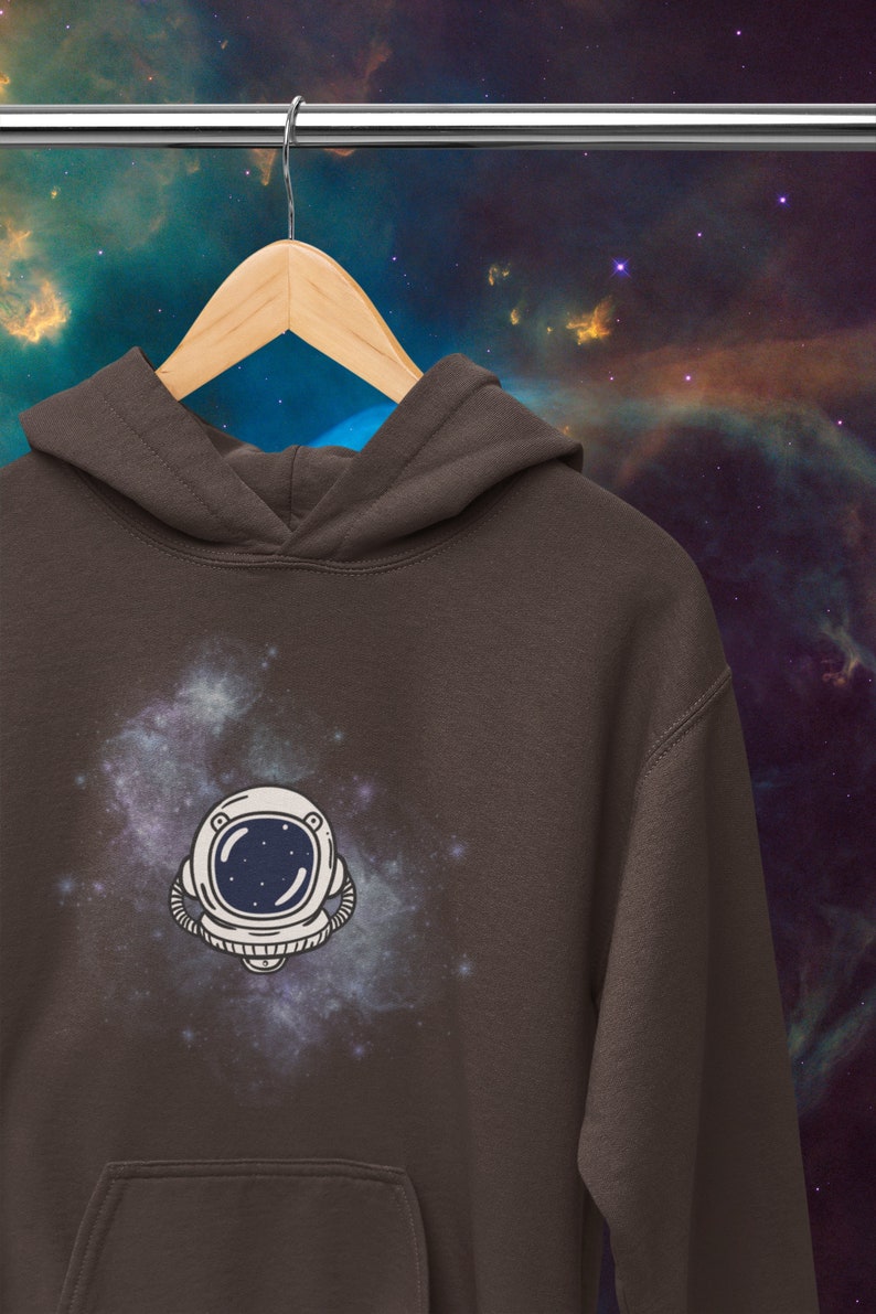 May include: A brown hoodie with a white astronaut helmet graphic against a galaxy background. The astronaut helmet has a dark blue visor and a white outline.