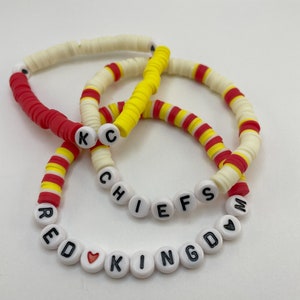 Könnte beinhalten: Drei Armbänder aus roten, gelben und weißen Perlen. Ein Armband schreibt "CHIEFS", ein anderes "RED KINGDOM", und ein drittes hat "KC" Perlen. Die Armbänder bestehen aus flachen, runden Perlen.