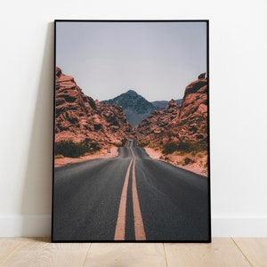 May include: A long, straight road with yellow lines down the center, leading through a canyon with red rock formations on either side. A mountain peak is visible in the distance.