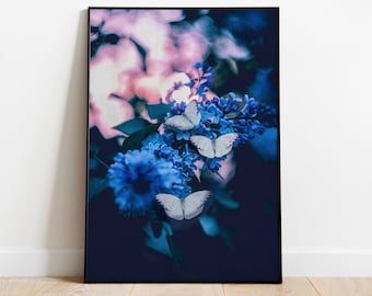 Puede incluir: Una impresión artística enmarcada que presenta flores azules y mariposas blancas. La imagen tiene una estética oscura y atmosférica, destacando el arreglo floral. El fondo es suavemente borroso con tonos rosas y morados, creando un efecto de ensueño.