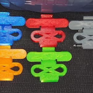 May include: Five 3D printed plastic pieces in different colours. The pieces are shaped like a figure eight with a flat top and bottom. The colours are blue, red, orange, green, and grey.