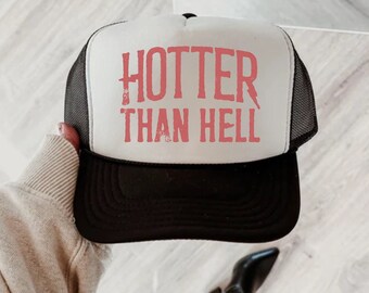 May include: A white trucker hat with a black mesh back. The hat has red text that says "Hotter Than Hell" in a distressed font.