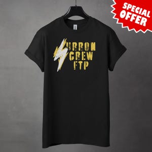 Puede incluir: Camiseta negra con un diseño gráfico amarillo y blanco desgastado. El diseño incluye un rayo y las palabras "URRON CREW FTP". La camiseta está colgada en una percha negra sobre un fondo gris. Una etiqueta roja de "SPECIAL OFFER" está en la esquina superior derecha.