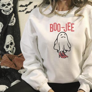 May include: White sweatshirt with a ghost wearing red shoes and the text "BOO-JEE" printed on the front.