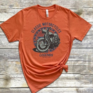 Op de afbeelding: Oranje T-shirt met een vintage-stijl grafische afbeelding van een motorfiets met de tekst "Classic Motorcycles Legends Never Die" in een cirkel met sterren.