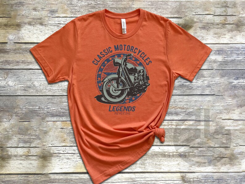 Op de afbeelding: Oranje T-shirt met een vintage-stijl grafische afbeelding van een motorfiets met de tekst "Classic Motorcycles Legends Never Die" in een cirkel met sterren.
