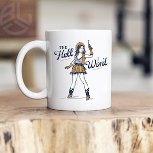 May include: White ceramic mug with a blue and yellow illustration of a woman in a cowboy hat holding a gun. The text "The Hell I Won't" is printed on the mug.