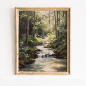 Puede incluir: Una pintura al óleo enmarcada que representa un paisaje forestal con un pequeño arroyo. La escena muestra árboles altos, follaje verde exuberante y luz suave filtrándose a través del dosel, todo dentro de un marco de madera clara.