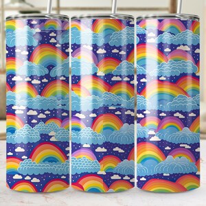 Pode incluir: Três copos de aço inoxidável com um padrão de arco-íris e nuvens. Os copos são azuis com arco-íris multicoloridos e nuvens brancas.