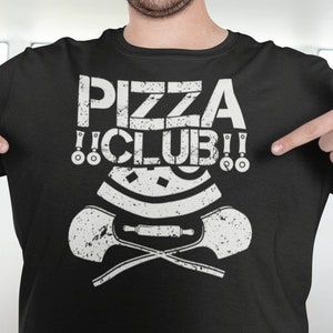 Può includere: Una maglietta nera con un design grafico bianco che dice "PIZZA !!CLUB!!" con una fetta di pizza, un matterello e una pala per pizza.