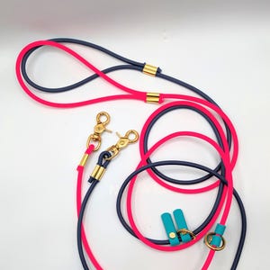 May include: A pink and navy blue dog leash with two gold clips and a gold ring. The leash is made of a durable, flexible material.