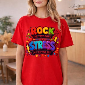 Peut inclure: T-shirt rouge avec l'inscription « ROCK THE TEST DON'T STRESS JUST DO YOUR BEST » dans un design coloré. Le motif comprend un crayon, une pomme, une règle et des étoiles.