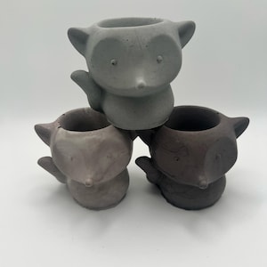 May include: Three small gray, brown, and light brown ceramic fox planters. The planters are shaped like foxes with a small hole in the top for planting.