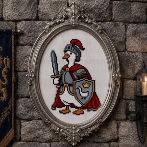 May include: A cross-stitch embroidery featuring a white goose dressed as a medieval knight, wearing a gray helmet with a red plume, a red cape, and gray armor. The goose holds a gray sword and a shield displaying a small white goose and a gold crown.
