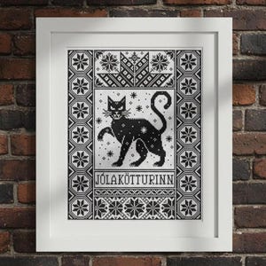 以下が含まれることがあります： 白いフレームに入った、黒と白のクロスステッチ。片足を上げた様式化された黒猫が、雪の結晶と幾何学模様に囲まれています。「JÓLAKÖTTURINN」の文字が下に表示されています。