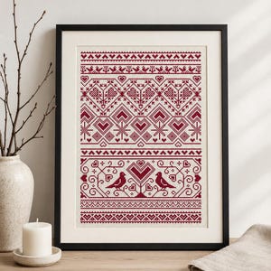 May include: A framed cross-stitch embroidery piece featuring a repeating pattern in deep red thread on a white fabric background. The design includes geometric heart motifs, stylized birds, and intricate floral borders within a black frame.
