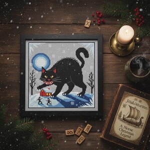 The Yule Cat cross stitch design embroidered on a light grey fabric, highlighting the snowy winter landscape and moonlight.