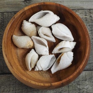 May include: A wooden bowl filled with white crystal-covered seashells. The shells are arranged in a circular pattern and have a natural, organic look.