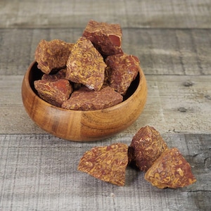 May include: A wooden bowl filled with rough, reddish-brown rocks with yellow veining. Several rocks are scattered around the bowl on a wooden surface. The rocks have a natural, textured appearance.