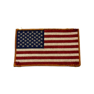 May include: A small embroidered American flag patch with a gold border. The flag is red, white, and blue.
