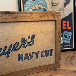 Puede incluir: Un letrero de madera con un logotipo azul y blanco que dice "Ayer's Navy Cut". El letrero est&aacute; enmarcado en un marco de madera r&uacute;stico.