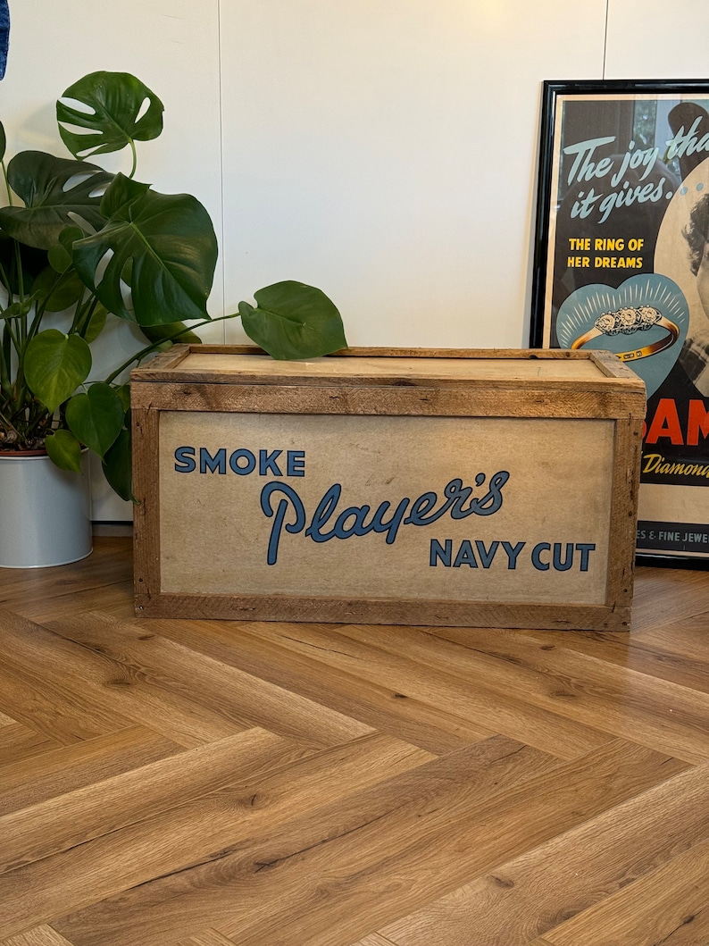 Puede incluir: Una caja de almacenamiento de madera con una etiqueta marr&oacute;n, beige y azul que dice "SMOKE Player's NAVY CUT".