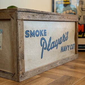 Puede incluir: Una caja de madera con una etiqueta blanca que dice "SMOKE Player's NAVY CUT" en letras azules.