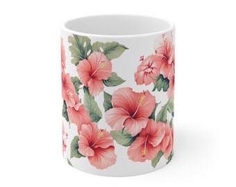 Könnte beinhalten: Eine weiße Keramiktasse mit einem Muster aus rosa Hibiskusblüten. Die Tasse ist mit rosa Hibiskusblüten und grünen Blättern verziert.