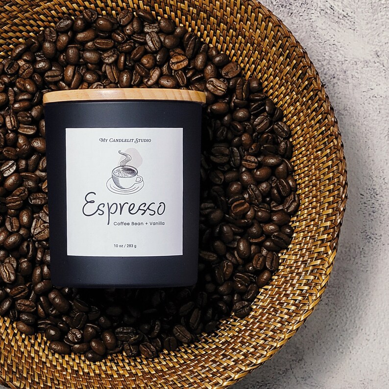 K&ouml;nnte beinhalten: Ein schwarzes Kerzengef&auml;&szlig; mit einem Holzdeckel. Das Etikett lautet "My Candlelit Studio" und "Espresso Coffee Bean + Vanilla" mit einer Zeichnung einer Kaffeetasse. Das Kerzengef&auml;&szlig; ist von Kaffeebohnen in einem geflochtenen Korb umgeben.