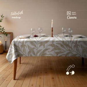 Op de afbeelding: Een rechthoekig tafelkleed met een beige en wit bladerpatroon bedekt een houten tafel. De tafel is gedekt met witte borden, wijnglazen en een brandende kaars. De tekst "Tablecloth mockup" staat linksboven.