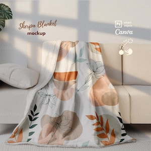 May include: A white sherpa blanket with an abstract floral design in orange, brown, and green. The blanket is draped over a white couch, with the text "Sherpa Blanket mockup" visible in the image.