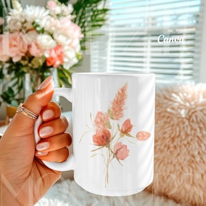 Trendy hand held mug mockup designed for Canva, featuring a 15oz ceramic mug with a delicate botanical illustration example. Styled in a cozy lifestyle setting with natural light and soft textures. Mug body is fully editable using Canva drag and drop while preserving realistic shadows. Ideal mugs mockup for creative sellers and modern mug mockups.