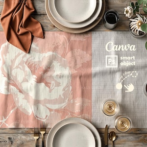 May include: A pink and white floral table runner with a checkered pattern on the right side. The runner is set on a wooden table with two place settings, each with a white plate and a gold knife and fork. The table is also decorated with a glass of wine, a napkin, and a potted plant.
