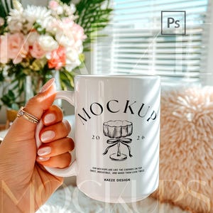 Hand held mug mockup featuring a 15oz ceramic coffee cup held naturally in hand, styled in a bright lifestyle interior with soft daylight. Trendy mug mockup showcasing realistic grip, ceramic reflections, and true scale. Editable mug body for custom artwork using PSD smart object and Canva drag and drop template. High quality mug mockups for modern 15oz mug mockup listings.
