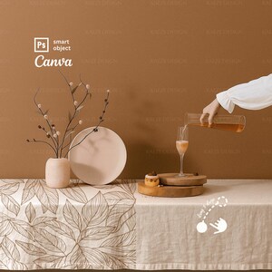Könnte beinhalten: Ein Stillleben mit einem Champagnerglas, das mit einem Getränk gefüllt wird. Ein kleiner Kuchen steht auf einem Holzständer. Eine Vase, ein Teller und ein dekorativer Zweig sind ebenfalls vorhanden. Die Szene spielt sich auf einer gemusterten Tischdecke ab.
