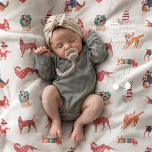 May include: A baby wearing a gray onesie and a beige turban, lying on a white blanket. The blanket is patterned with illustrations of dogs wearing holiday attire. A pacifier is in the baby's mouth.