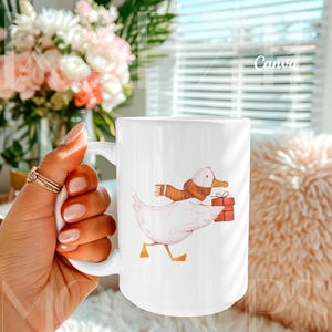 Hand held mug mockup optimized for Canva showing a 15oz ceramic mug with a playful illustrated duck artwork example. Clean lifestyle background with natural lighting and realistic hand positioning. Editable mug body allows easy design replacement via Canva drag and drop. Trendy mug mockups perfect for cute, illustrated, or gift-style 15oz mug mockup designs.