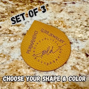 May include: Three tan leather tags in a teardrop shape, each bearing the text "PERMANENT PROJECT LITTLE DIPPER LLC" and "LUXE JEWELRY" in black. The tags also feature the initials "pld". The text "CHOOSE YOUR SHAPE & COLOR" is also visible.