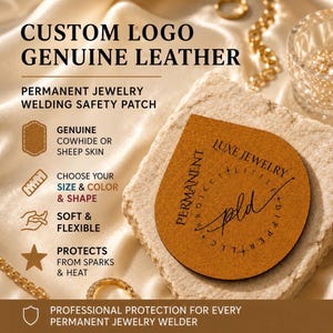 May include: A tan, semi-circular genuine leather welding safety patch for permanent jewelry. The patch features black printed text including "LUXE JEWELRY" and "pld" with a circular border. It is designed to protect skin from sparks and heat.