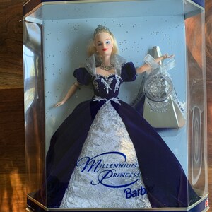 May include: A Barbie doll dressed in a blue velvet gown with silver accents. The doll is holding a silver crystal ball and is standing in a clear plastic display case. The box is labeled "Special Millennium Edition" and "Millennium Princess Barbie".
