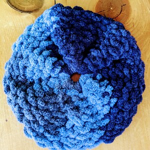 Peut inclure: Un chouchou fait à la main dans des tons de bleu, du clair au foncé. Le chouchou est fait d'une matière douce et texturée et est de forme circulaire. Le fond est une surface en bois brun clair.