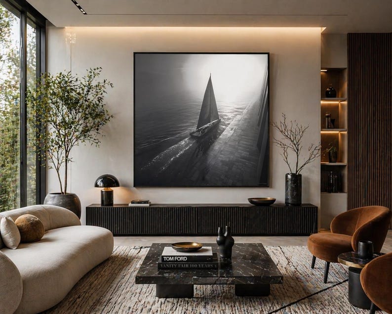 May include: A modern living room with a large black and white framed sailboat art piece. The room features a black console, a marble coffee table, and a curved beige sofa. Brown accent chairs and a patterned rug complete the space.
