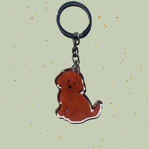 May include: A keychain featuring a brown dog illustration. The dog is sitting with its tail curled. The keychain has a silver-colored ring and chain. The dog illustration has a white outline.
