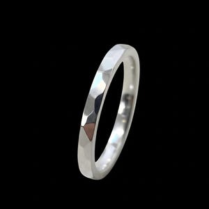 May include: A silver ring with a faceted design. The ring is thin and has a textured surface, reflecting light. The ring is set against a black background, highlighting its metallic sheen. A piece of jewelry.
