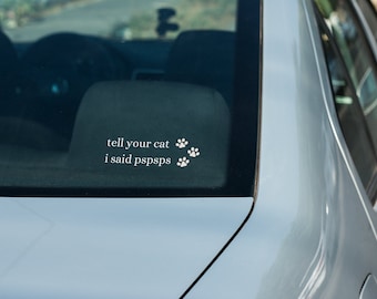 May include: A silver car with a white sticker on the rear window that says "tell your cat I said pspsps" with four paw prints.