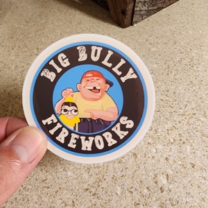 May include: A round sticker with a blue, black, and white design. It features a cartoon image of two people, one with a red hat and the other with glasses. The text "BIG BULLY FIREWORKS" is written in a black circle around the image.
