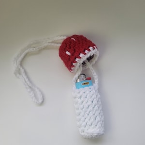 Puede incluir: Un soporte para encendedor hecho a mano con ganchillo en forma de seta. El sombrero de la seta es rojo con lunares blancos y un ribete blanco. El soporte para encendedor es blanco y tiene una correa. Un encendedor BIC azul y blanco está dentro.